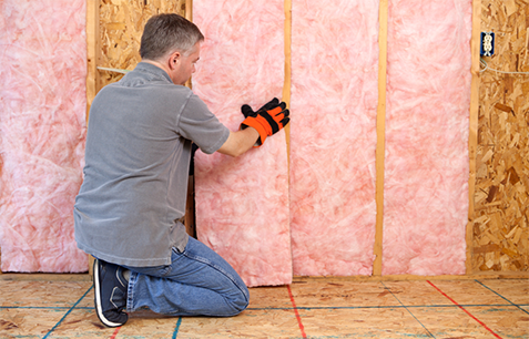Technician installing pink fiberglass batt home insulation in walls
