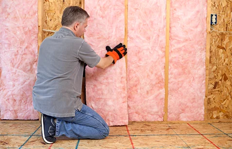 Technician installing pink fiberglass batt home insulation in walls