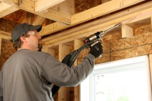 Technician air sealing the space between the ceiling and wall in a new construction home.