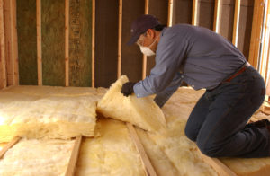 Technician installing fiberglass insulation in attic floor