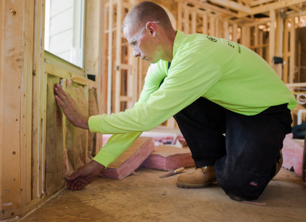Technician installing insulation in a wall under a window in a home under construction.